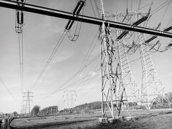 Low angle view of electricity pylons on field against sky