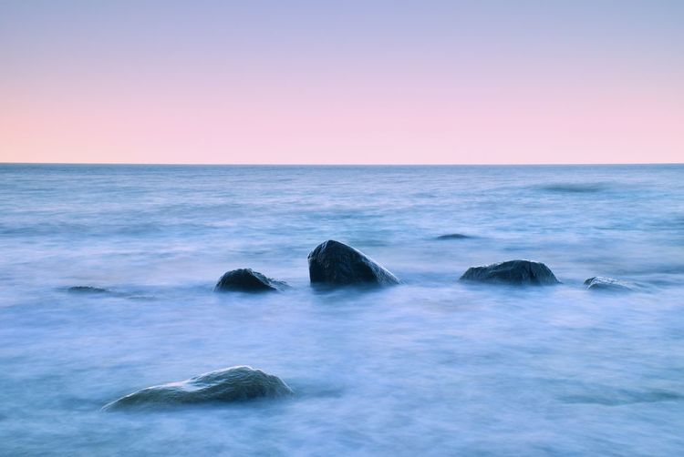 Morning at sea. big boulders sticking out from smooth wavy sea. pink horozon with first hot sun rays