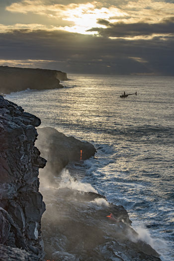High angle view of sea splashing against rocks during sunset