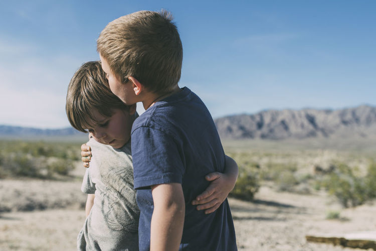 Boy kissing brother while standing at joshua tree national park against sky during sunny day