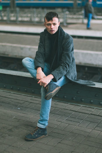 Full length of young man sitting at railroad station