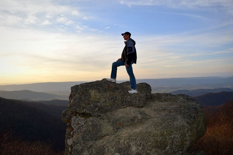 Full length of man standing on rock against mountains during sunset