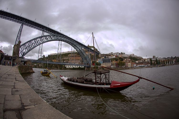Boat sailing in douro river against bridge and cloudy sky in city