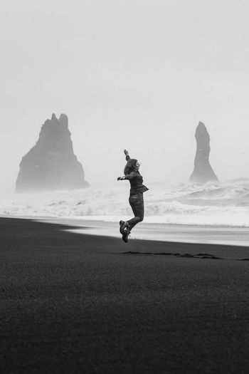 Happy tourist jumping on black northern monochrome beach scenic photography