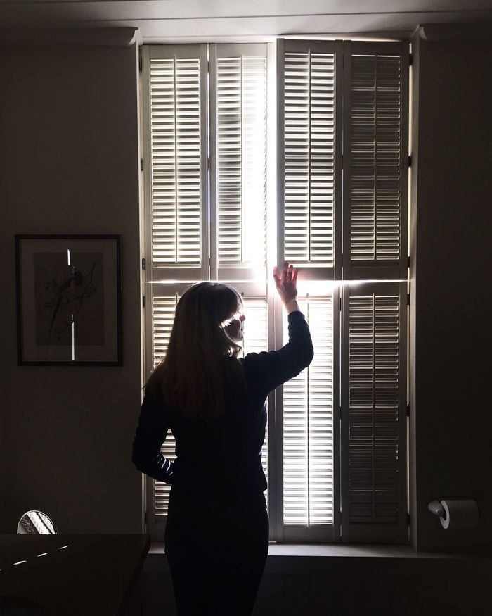 Rear view of woman holding window shutter at home