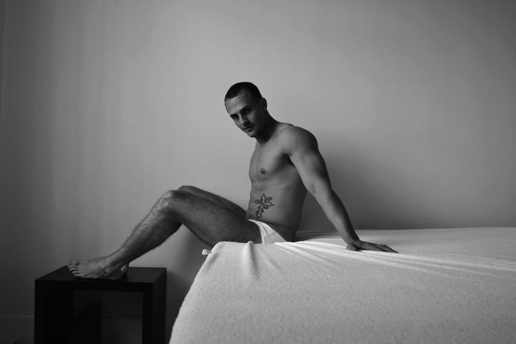 Portrait of model wearing underwear while sitting on bed against wall