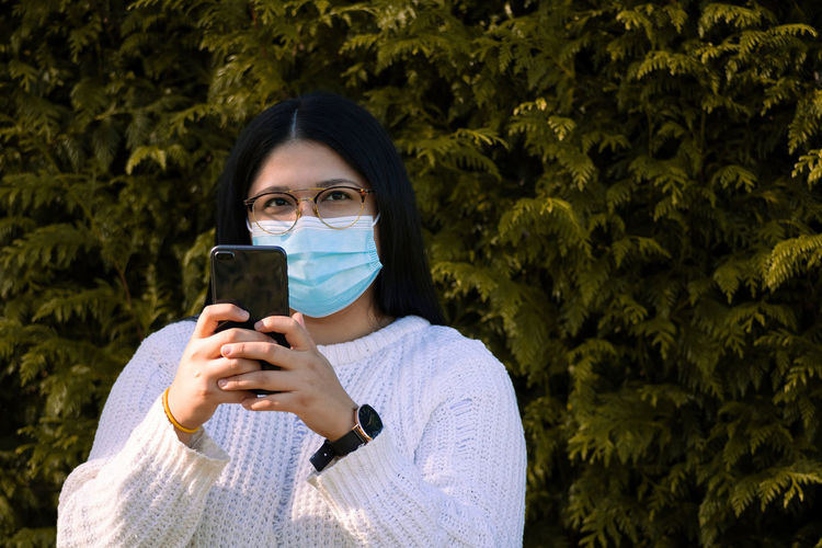 Woman with a surgical mask using the mobile in social networks. woman in the park.