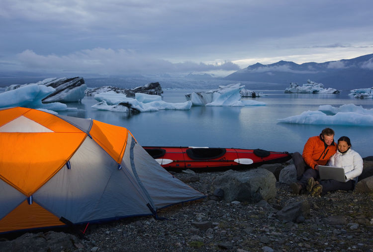 Couple looking at laptop on campsite by glacier lagoon in iceland