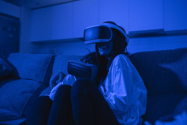 Mother sitting with daughter using virtual reality glasses in blue illuminated room