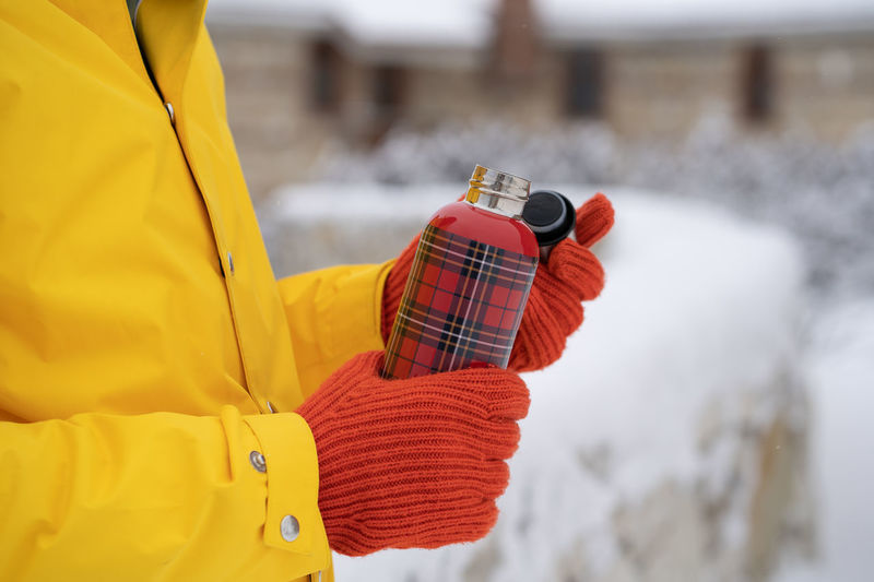 Closeup hands of man in jacket wearing winter gloves with steel thermos for storing hot drink