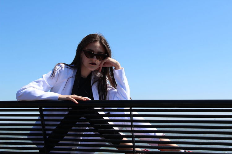 Confident girl sitting by railing against clear blue sky