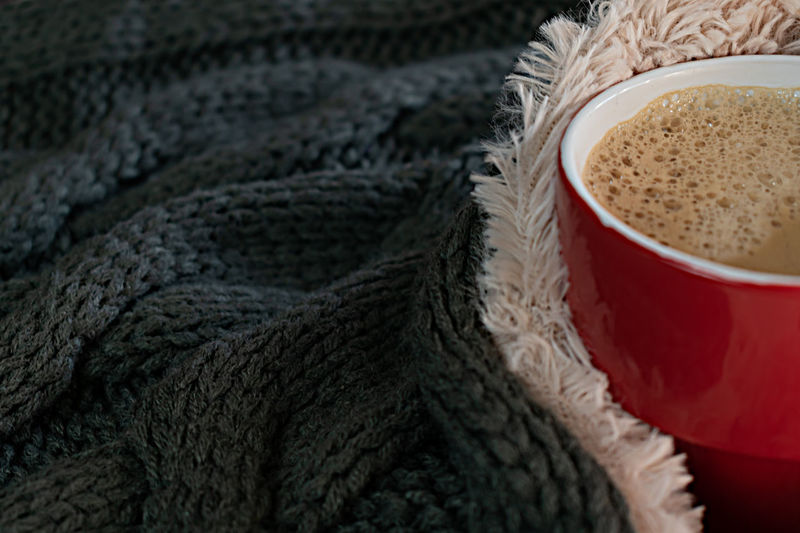 Close up of cup of coffee wrapped in a warm kniteed scarf or blanket