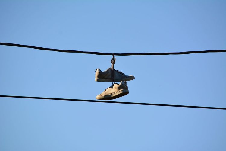 Low angle view of shoes hanging on cable against clear blue sky