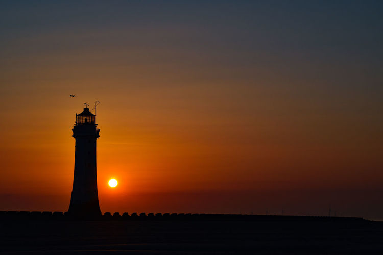 Silhouette lighthouse against orange sky