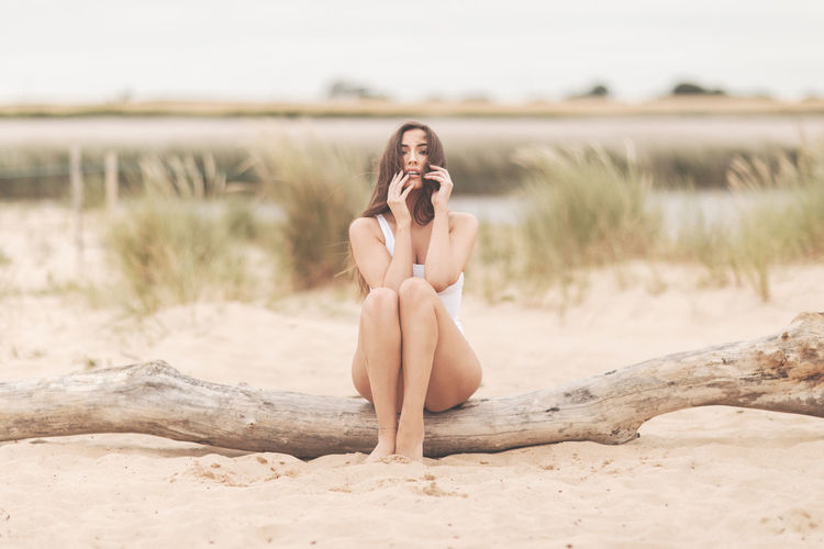 Portrait of young woman sitting on tree trunk at beach