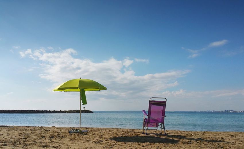 Parasol and deck chair on beach against sky 