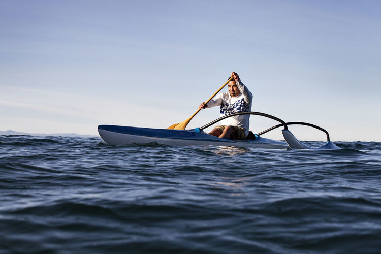 Mature man rowing outrigger on sea against clear sky during sunny day