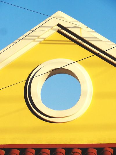 Low angle view of hole on yellow pediment against clear sky