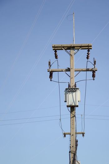 Low angle view of electricity transformer against clear blue sky