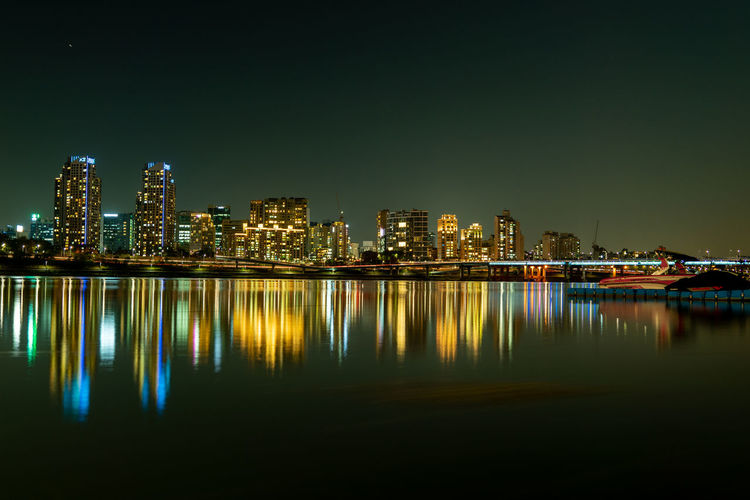 Illuminated buildings by river against sky at night