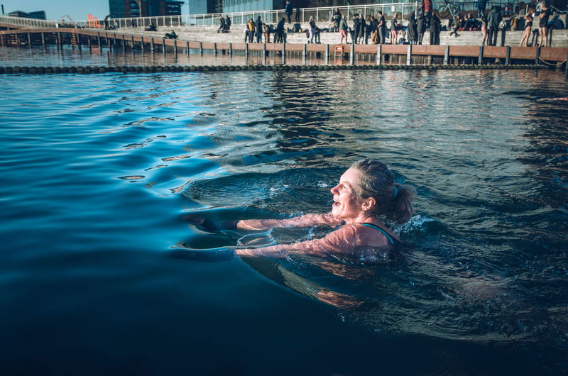 Mature woman swimming with sun shining in freezing water in denmark