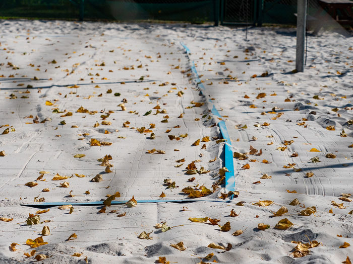 Closed beach volleyball court in fall season. autumn and fallen leaves on white playground sand.