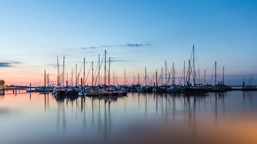 Sailboats moored in harbor against sky during sunset