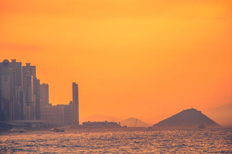 Scenic view of sea by buildings against orange sky