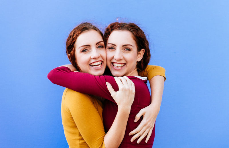 Portrait of smiling siblings embracing against blue background