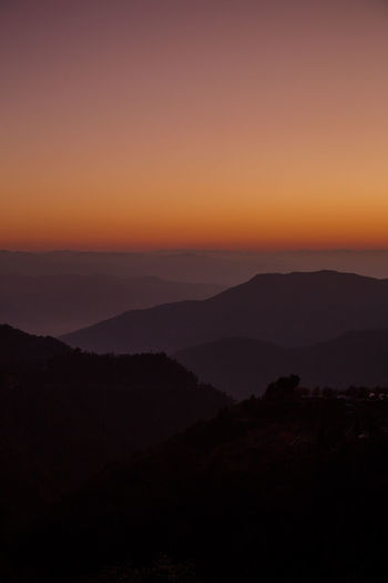 Scenic view of silhouette mountains against orange sky