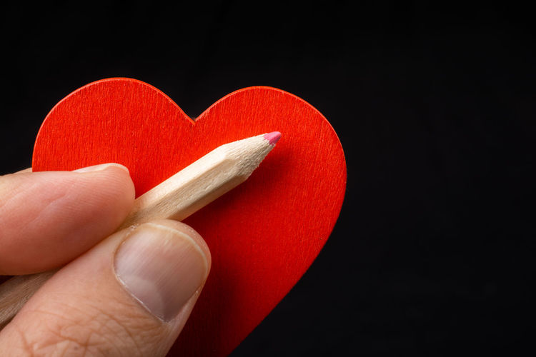 Close-up of hand holding heart shape over black background