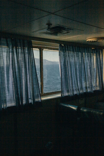 The passenger seats on the ferry boat, view through the window and curtains  behind which is sea.