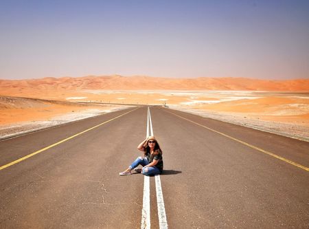 Full length of woman sitting on country road amidst desert during summer