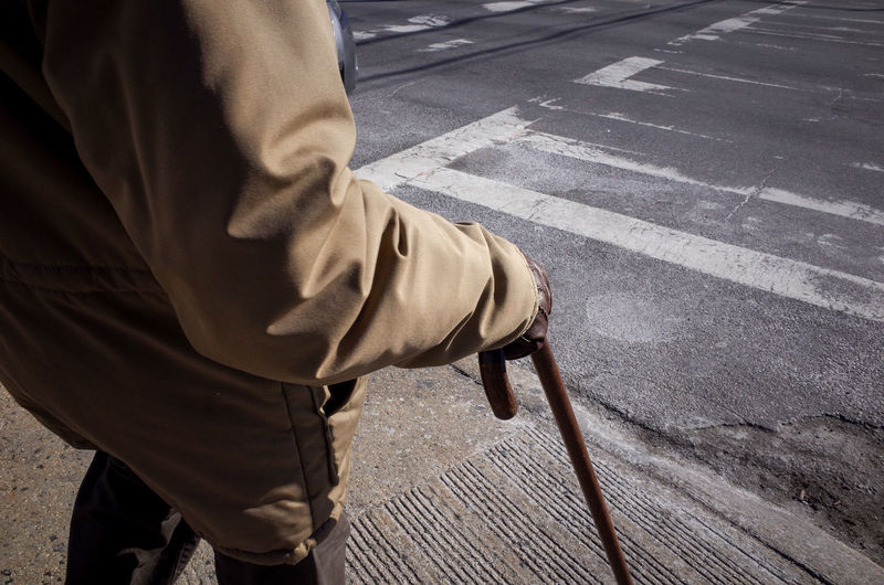 Midsection of senior man standing with walking cane on sidewalk
