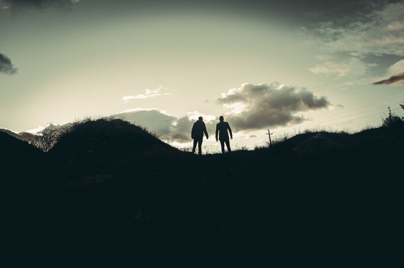 Silhouette men standing on mountain against sky during sunset