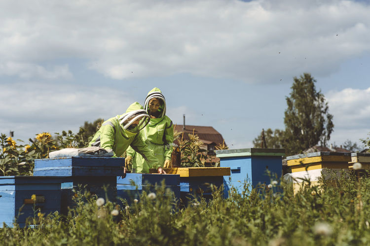 Beekeepers standing by wooden boxes under cloudy sky