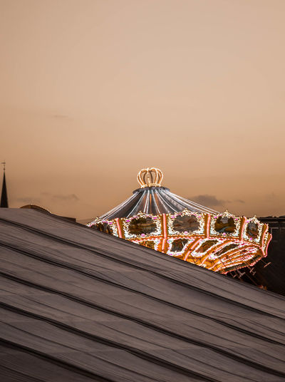 Illuminated carousel against sky at sunset
