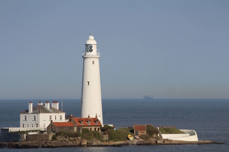 Lighthouse by sea against buildings against clear sky