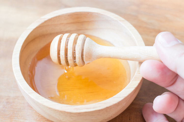 Close-up of hand holding honey dipper on table