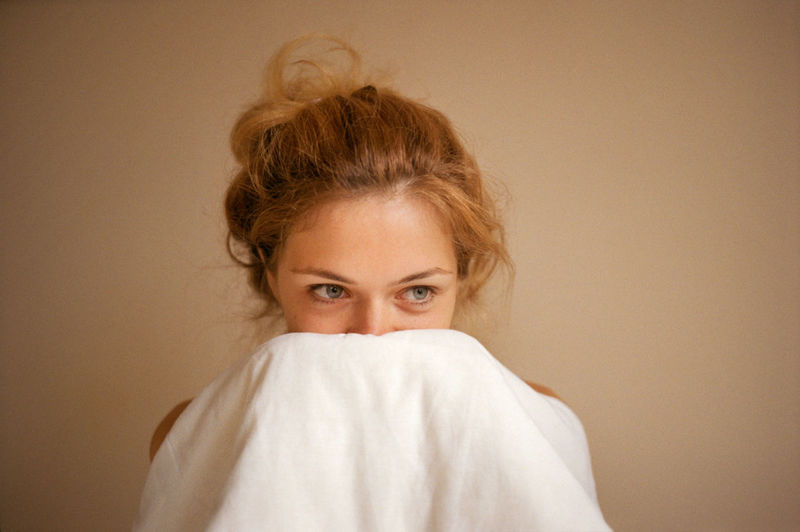 Young woman covers her face with a blanket close-up of the face.