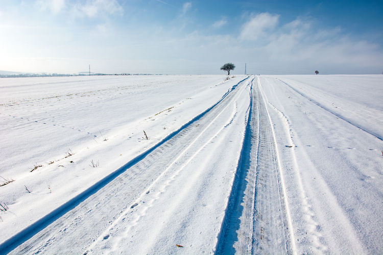 Tire tracks on snow covered land against sky