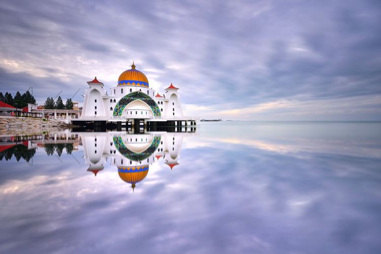Reflection of mosque on sea against sky during sunrise