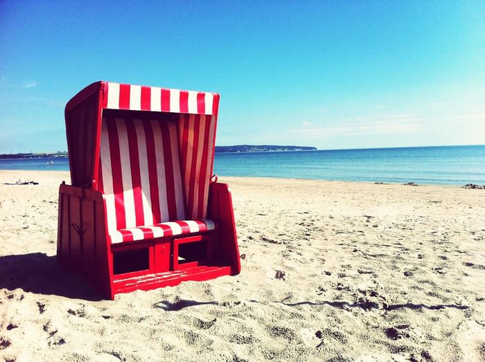 Red hooded chair at beach against blue sky on sunny day