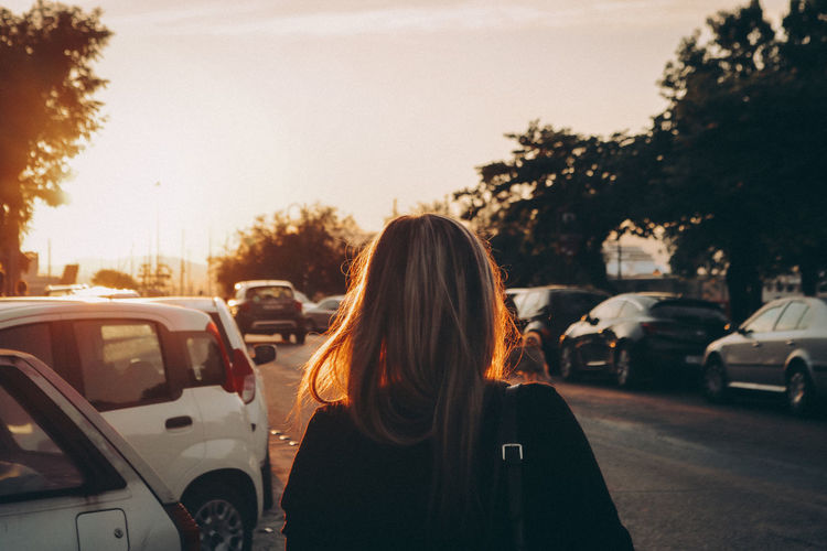 Rear view of woman standing on street against sky during sunset