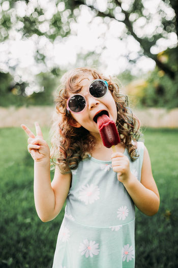 Young girl eating a popsicle and giving a peace sign outside