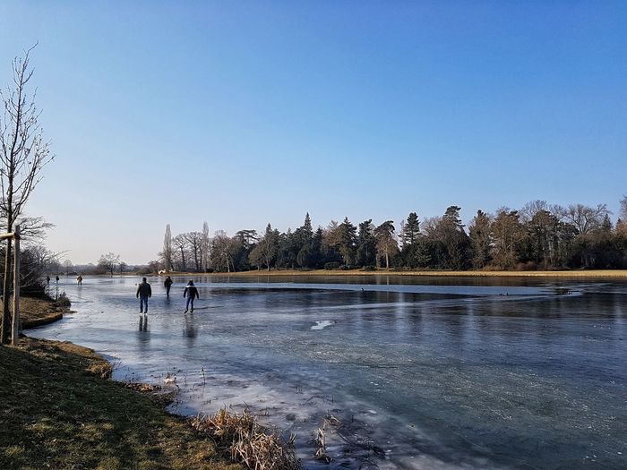 People walking on frozen lake against clear sky