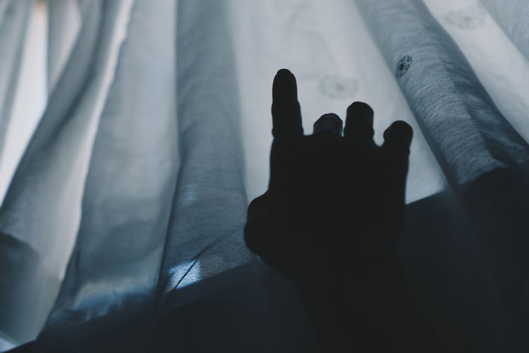 Close-up of silhouette hand gesturing by curtain