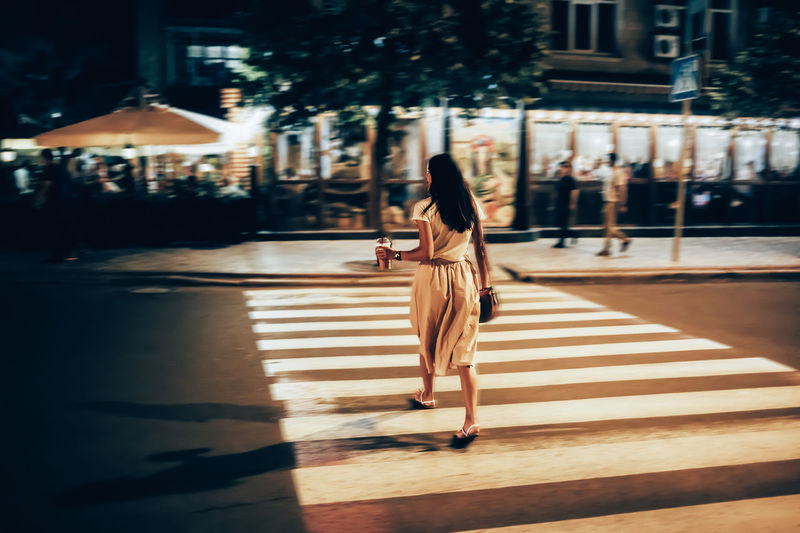 Woman with smoothie crossing street at night