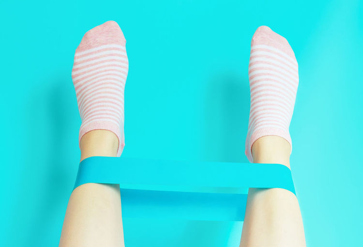 Female legs hold elastic fitness rubber band on a blue background.