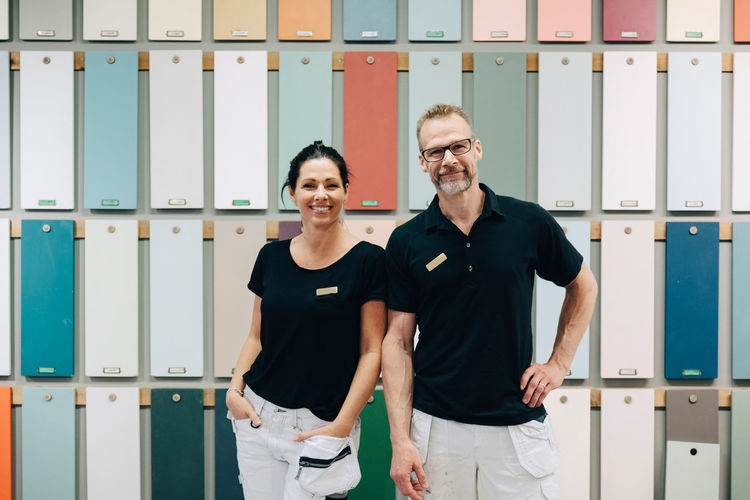 Portrait of smiling sales employees standing against multi colored wall in store